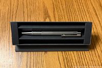 Metal Lamy ball point pen in original black box on wood surface.