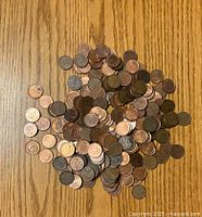 A pile of loose U.S. one-cent coins scattered on a wooden surface showing various toning and usage levels.