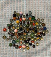 Top-down photo showing about 90 variously colored glass marbles laid out on a textured blue and white background.