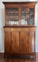 Front view of the antique wooden cabinet showing the upper glass doors with decorative muntins and lower wooden doors.