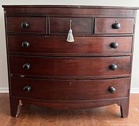 Front view of an antique wooden dresser showing four large curved drawers and three smaller drawers at the top. The dresser has a dark reddish-brown finish with rounded wooden knobs and a tassel on the central keyhole.