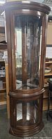 Full view of corner curio cabinet showing wooden frame, curved glass front, and base section.