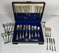 Full view of the cutlery set showing all pieces arranged around and inside the wooden case with blue velvet lining.