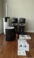 Front view of four humidifiers: one white tall Lacidoll ultrasonic humidifier, two identical black Honeywell cool moisture humidifiers, one black Honeywell warm mist humidifier, user manuals, and two filter packages on wood floor.