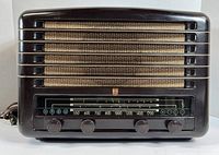 Front view of vintage Philips electric radio showing beige fabric grille and tuning window with frequency scale and control knobs.