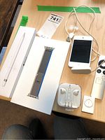 Overview of lot items on desk: Apple Pencil box, Apple Watch band box, Apple EarPods case, iPod Touch with dock, Apple TV remote, iPod shuffle.