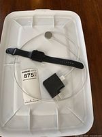 Full top view of Apple Watch with black sport band laid out on plastic tray along with charging cable and power adapter.