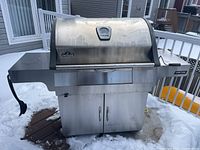Full front view of stainless steel Napoleon charcoal grill on snow-covered deck