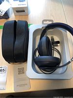 Headphones resting in original plastic tray alongside semi-rigid case and documentation card on wood desk