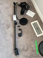 Overview of boom arm, microphone, pop filter, manual and clamp laid out on carpet