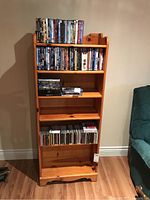 Front view of the wooden bookshelf displaying DVDs and CDs on shelves for scale.
