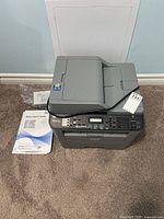 Printer with manual, CD and power cord on carpet against wall