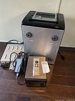 Overview of all three devices on floor: tall silver slot-load drive, black QNAP NAS, grey Chase terminal server with connectors