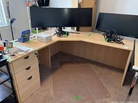 Corner office desk shown with dual monitors and various items on top, corner design with drawers on left side