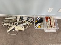 Overview of a large quantity of various power bars and extension cords, mostly white, polled together on carpet floor.