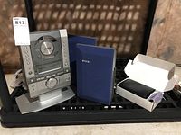 Sanyo portable CD/AM/FM stereo radio with two blue manuals and a small box containing an accessory, shown on a black shelf against a brown background.