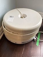Overall view of Nesco American Harvest Gardenmaster food dehydrator with cover on, showing electrical cord and unit shape.