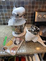 Stand mixer on countertop with stainless steel bowl, recipe booklet and shredding attachment housing