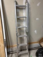 Full view of folding aluminum ladder in folded position against wall.