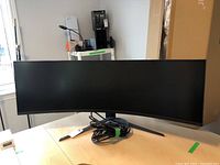 Front view of 49-inch curved monitor on V-shaped stand with HDMI cable coiled at base