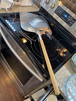 Two pizza lifters on a stovetop. One is a large rectangular metal peel with a wooden handle, the other is a smaller round metal peel with a plastic handle.