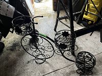 Overall right-side view of black metal tricycle plant stand resting on garage floor