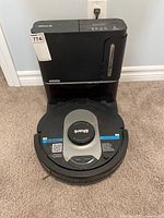 Front view of robot vacuum docked at charging tower on carpeted floor
