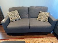 Front view of grey loveseat with two patterned throw cushions