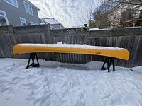 Full side view of yellow Swift Prospector 17 canoe mounted on two black saw horses in snow