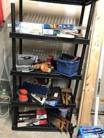Full view of the black plastic shelving unit holding assorted tools including power tools, hand tools, and boxed items.