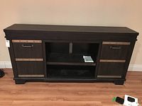 Front view of modern wood TV stand with two cupboards and center open shelf, dark finish with metal accents.