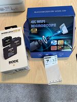 Two product boxes on tabletop: RODE Wireless Go II box and 4K WiFi microscope box