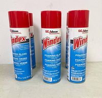 Group of six SC Johnson Windex Foaming Glass aerosol cans with red caps, standing upright on a surface against a white wall.