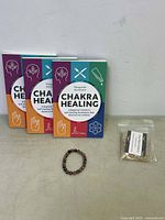 Four chakra healing books lined up next to a beaded bracelet and a small bag of resin incense.