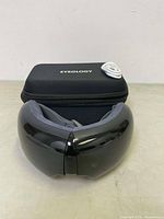 Eyeology eye massager with case and USB cable on a plain surface.