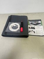 Photo of folded black grounding mat with small perforations, white cable and grounding rod with red handle, alongside instruction manual.