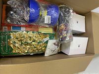 Top view of box showing a pack of gold and green Christmas bows, blue and white disposable cups, and two white boxes.