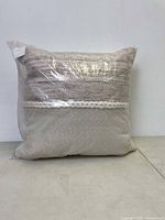 Front view of the packaged outdoor pillow showing knit texture and braided detail in beige tones.