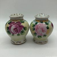 Front view of pair of antique hand painted salt and pepper shakers, showing rose floral design and gold accents on ceramic bodies.