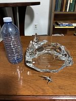 Clear Baccarat crystal glass sculpture with two peak-like peaks, shown next to a water bottle for size comparison. Small metal figure skater shown detached in front.