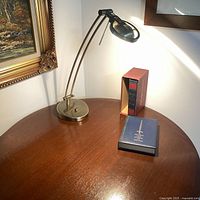 Desk lamp on wooden round table with a book and a book holder nearby, showing lamp off and on states and height.