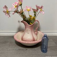 Large pink ironstone pottery pitcher filled with flowers sits inside matching wash basin, shown next to an average size water bottle for scale.