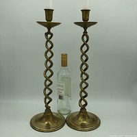 Pair of vintage brass spiral twist candlestick holders side by side with a wine bottle for scale, taken against a plain background.