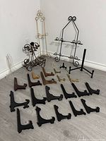 Wide view of the lot showing black, gold, wooden, and acrylic plate stands spread on floor