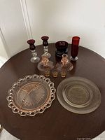 Lot of vintage coloured glass items arranged on a table, showing overall quantity and variety including plates, candlesticks and glass containers.