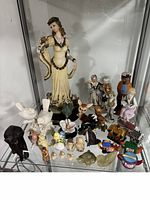 Full lot of vintage figurines including a large woman figurine, several animal and character figurines, and small collectible toys on a shelf
