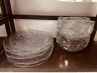 Photo showing three clear glass bowls stacked, each with repeated embossed grape cluster patterns around the exterior sides.