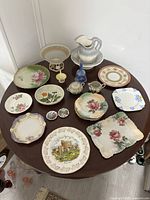 Top view of a round table filled with vintage decorative plates, bowls, pitchers, and small ceramic items with floral patterns and gold accents.