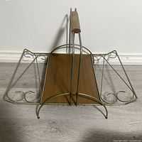 Top angled view showing metal frame, wooden handle, and wooden base of mid century modern magazine rack or record holder with curved wire sides.