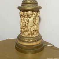 Close-up of porcelain cherub figures in relief on the lamp base with gold finish